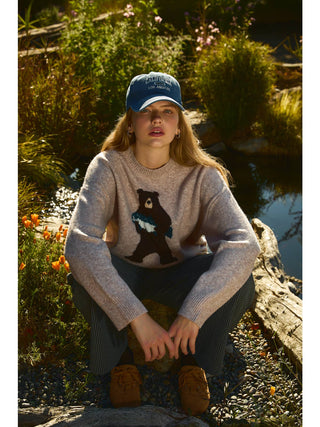 Model seated outdoors wearing oversized crew neck sweater with bear graphic design
