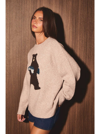 Model wearing oversized taupe crew neck sweater with bear graphic on front, paired with denim shorts