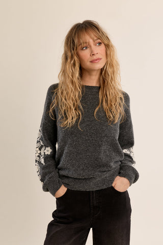 Woman wearing a dark grey knitted sweater with floral embroidery detail on sleeves