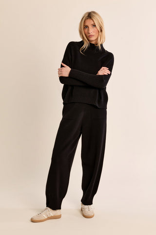Woman wearing a black knitted turtleneck sweater with ribbed cuffs and hem, arms crossed