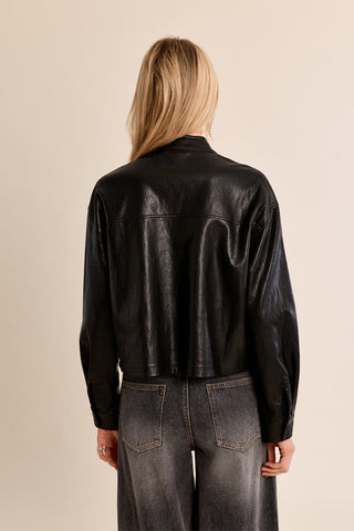 Back view of a woman wearing a cropped faux leather overshirt with long sleeves and wide-leg jeans