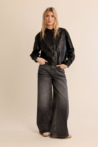 Model wearing a black faux leather overshirt with front pocket and button closure