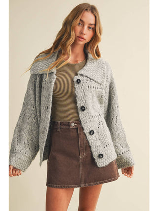 Model wearing open-front eyelit knit cardigan sweater with black buttons and wide collar