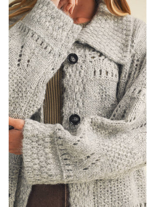 Close-up detail of chunky knit cardigan with dark buttons and eyelit texture pattern