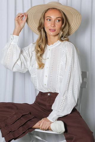 Woman seated wearing long puff sleeve cotton eyelet blouse with wide-brim straw hat and brown ruffled skirt